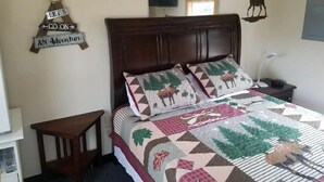Une chambre à coucher avec un lit en bois, deux oreillers à motifs animaliers, une petite table de chevet et un téléviseur fixé au mur.