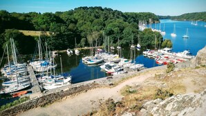 Een jachthaven met veel boten afgemeerd, omgeven door weelderige begroeiing en heuvels.