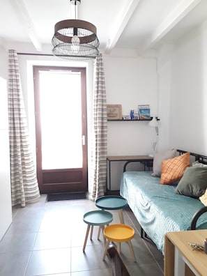 Une petite pièce bien éclairée, avec un lit, un bureau, une chaise et un luminaire suspendu.