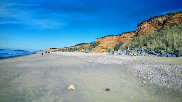 Een strand met heldere lucht, rotsachtige kliffen en een kiezelstrand.