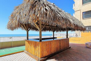 Relax in a shaded beachside retreat with a bench and table nearby, surrounded by a fence and a paved walkway leading to the beach.