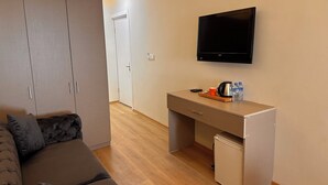 Quarto de hotel moderno com sofá, escrivaninha, televisão e minibar.