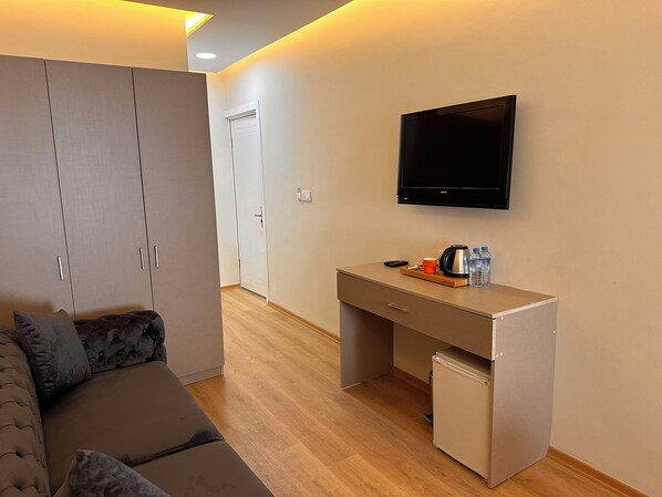 Une chambre d’hôtel moderne équipée d’un canapé, d’un bureau, d’une télévision et d’un mini-réfrigérateur.