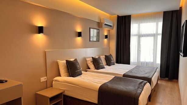 Quarto de hotel com duas camas, uma mesa de cabeceira, televisão e ar condicionado.