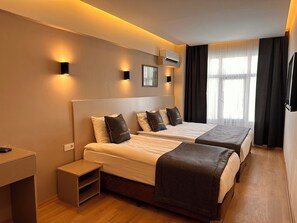 A hotel room with two beds, a bedside table, a TV, and an air conditioning unit. - Harran Hotel (Istanbul)