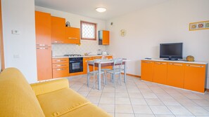 A compact kitchen with orange cabinets, a dining table with chairs, a stove, and a television on a cabinet.