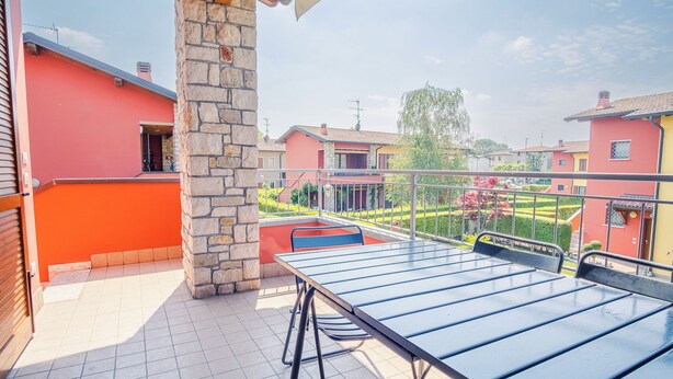 A balcony with a table and chairs, overlooking a residential area with houses and a well-maintained garden. - Garda Orange Apartment (Desenzano del Garda)