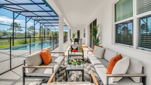 A covered outdoor seating area with a pool view, modern furniture, and large windows.
