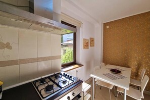 A compact kitchen with a gas stove, a window with a view, and a dining area with a table and chairs. - Spacious Apartment In The Centre Of The Capital (Bucharest)