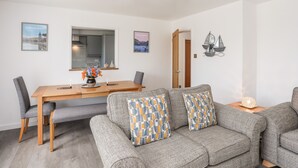 A modern living room with a wooden dining table, grey sofa, and decorative pillows. - 31 Beach Road (Porthmadog)