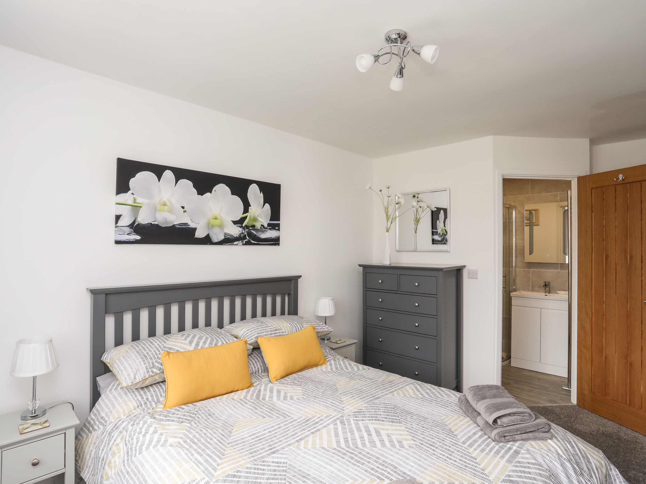 A bedroom with a bed, a nightstand, a dresser, a mirror, and a door leading to a bathroom.