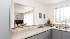 A modern kitchen with a large window, a built-in sink, and a clock on the wall. - 31 Beach Road (Porthmadog)