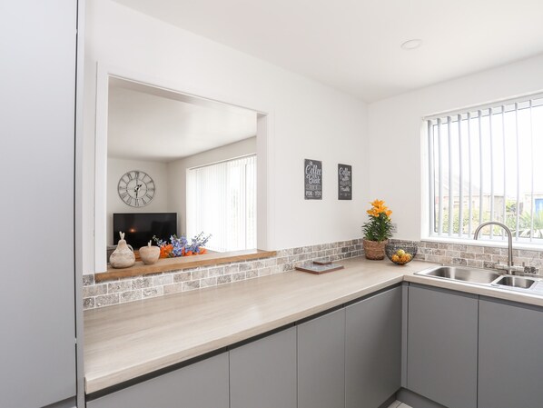 A modern kitchen with a large window, a built-in sink, and a clock on the wall. - 31 Beach Road (Porthmadog)