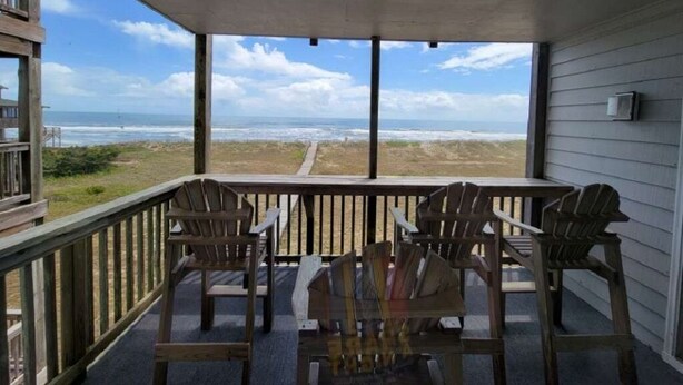 Un portico coperto con vista sulla spiaggia, sedie di legno e un tavolo.