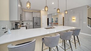 A modern kitchen with a large island, bar stools, and pendant lighting.