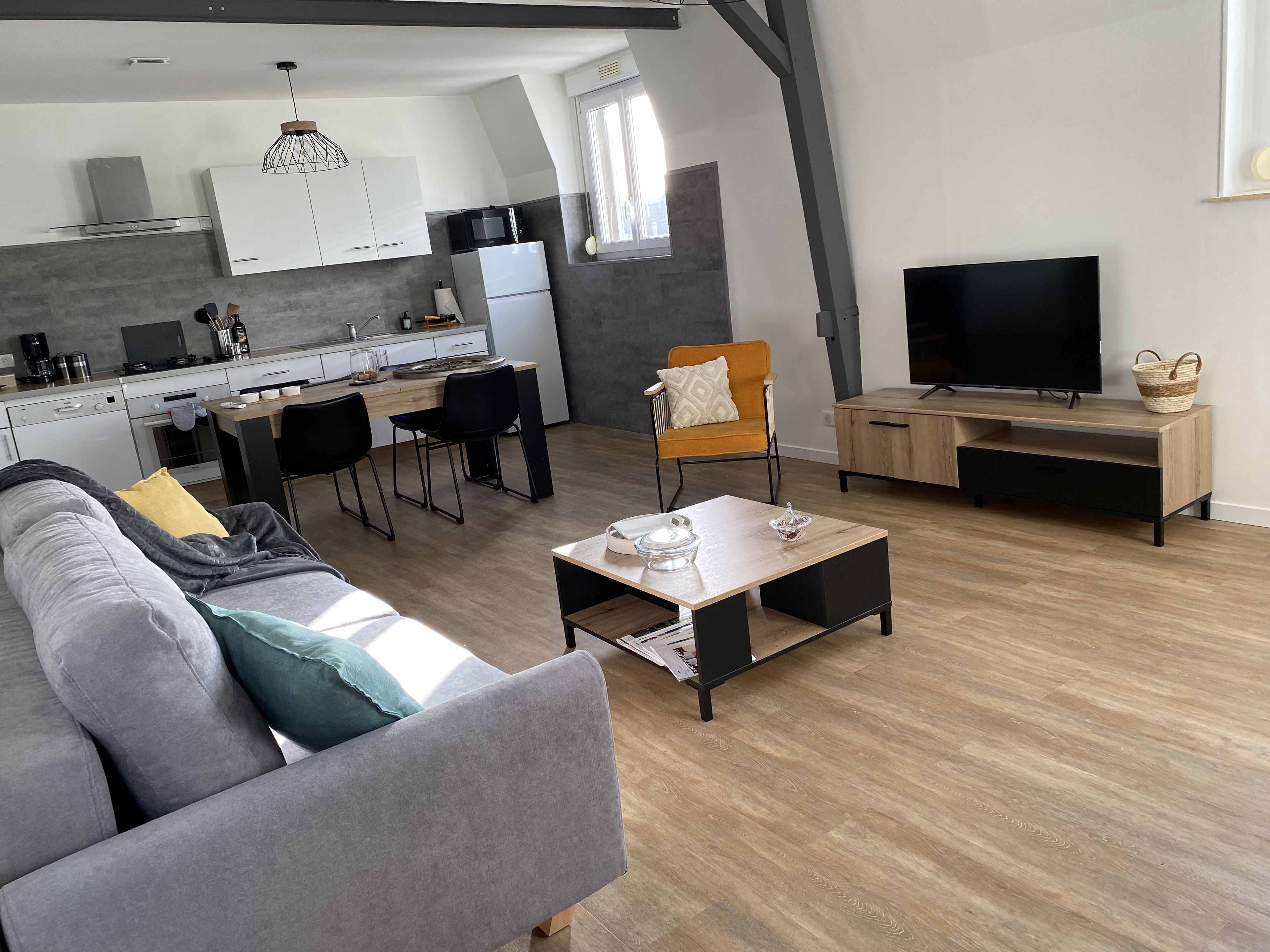 A modern living space with a sofa, coffee table, TV, and kitchen area including a microwave and refrigerator.