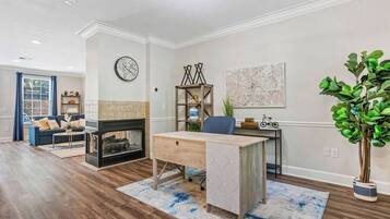 A modern living room with a fireplace, a desk, and a large plant.