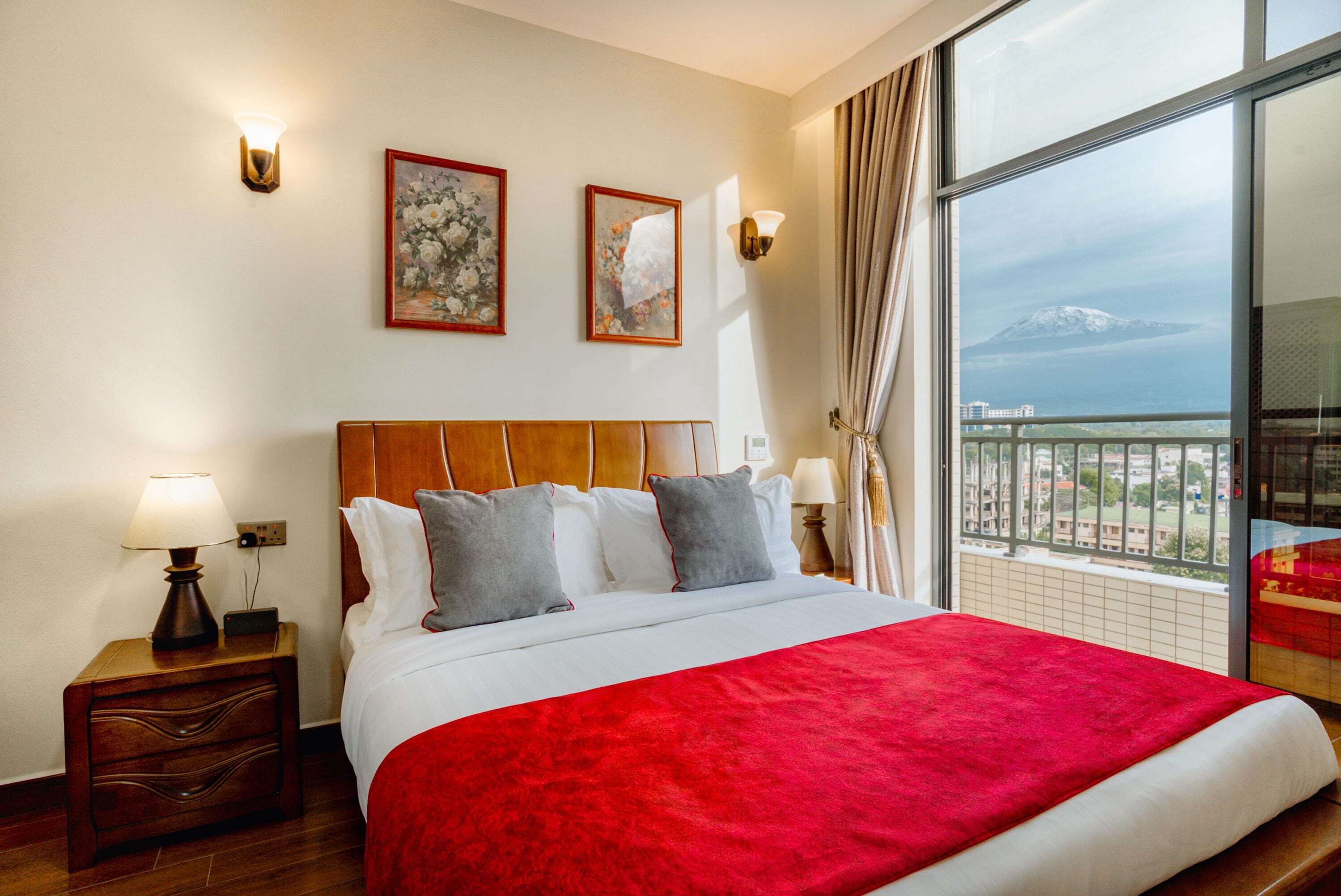 A hotel room with a large bed, two wall-mounted lamps, and two framed floral paintings.