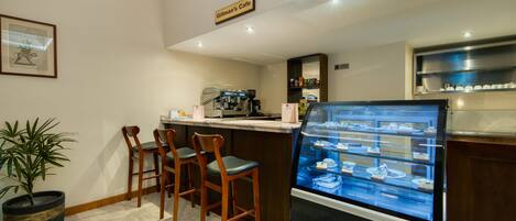 Una cafetería con una vitrina de pasteles, sillas de madera, una máquina de café y un letrero que dice "Gillman's Cafe".