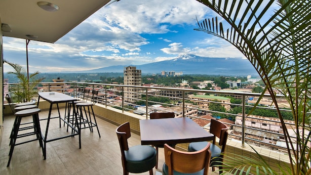 A balcony with a table and chairs, overlooking a cityscape with buildings and a mountain. - Kibo Palace Hotel Moshi (Moshi)