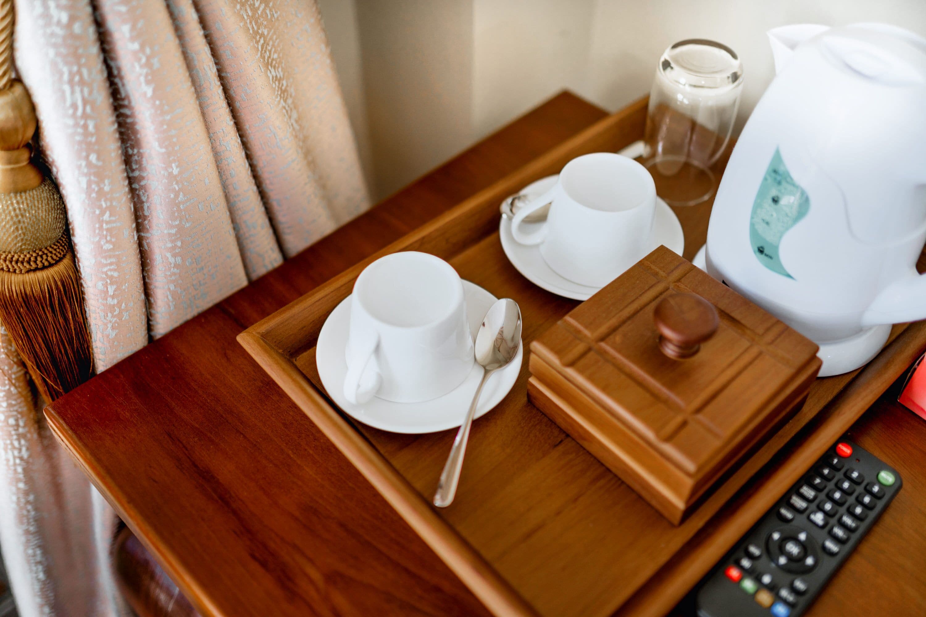 Una bandeja de madera con una taza blanca, un plato y una tetera sobre una mesa de madera.