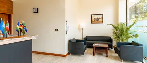 A reception area with a reception desk, a black sofa, a small table, a lamp, a potted plant, and flags on the wall.
