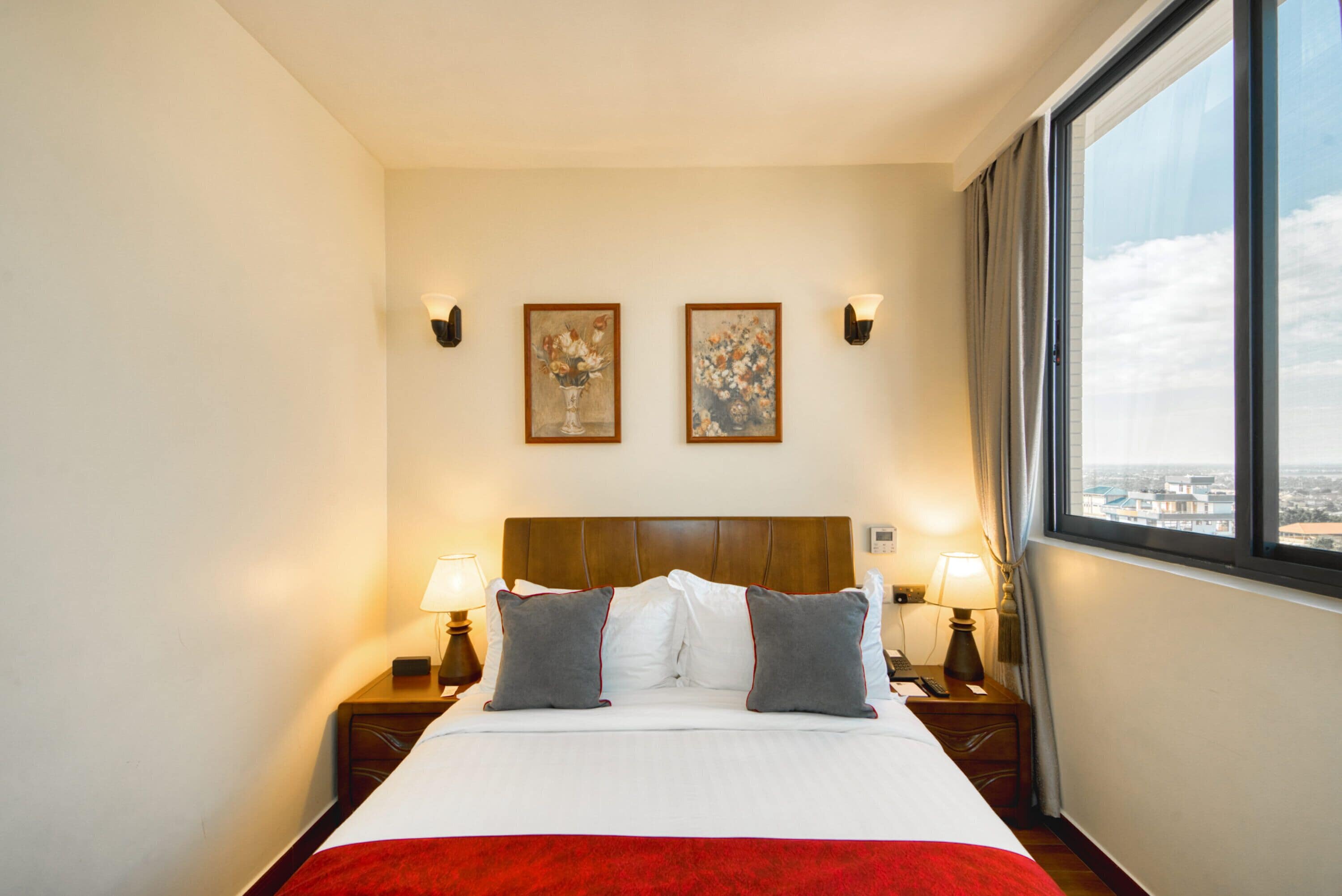 A hotel room with a large bed, two wall-mounted lamps, and two framed paintings above the bed.