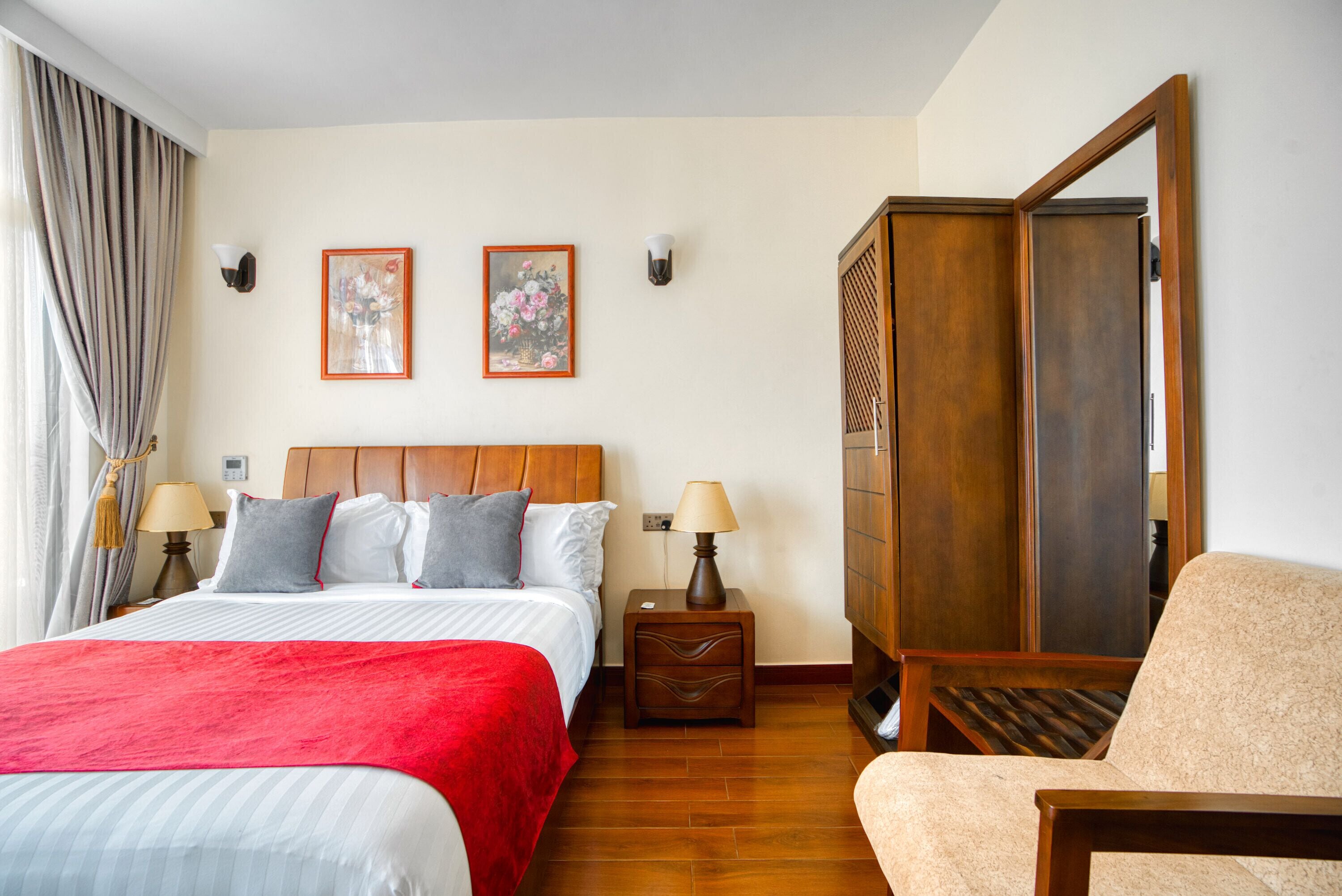 Hotellihuone, jossa on suuri sänky, kaksi yöpöytää valaisimineen, puinen vaatekaappi ja tuoli.