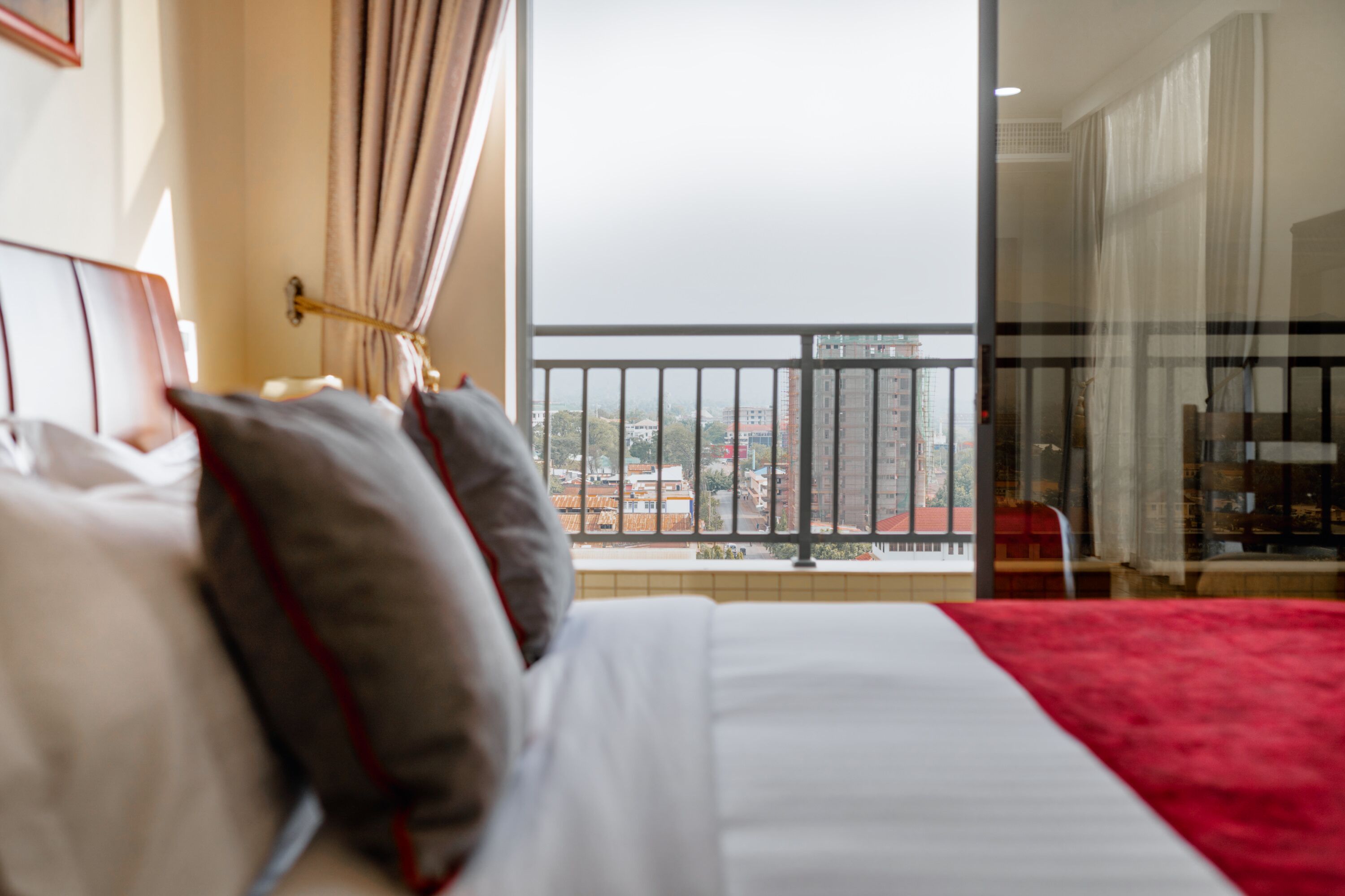 Una habitación de hotel con una cama, vistas a la ciudad desde un balcón y una alfombra roja.