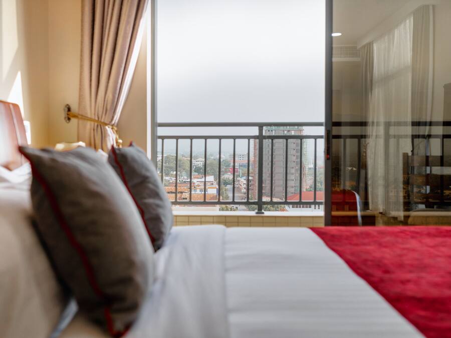 Una habitación de hotel con una cama, vistas a la ciudad desde un balcón y una alfombra roja.