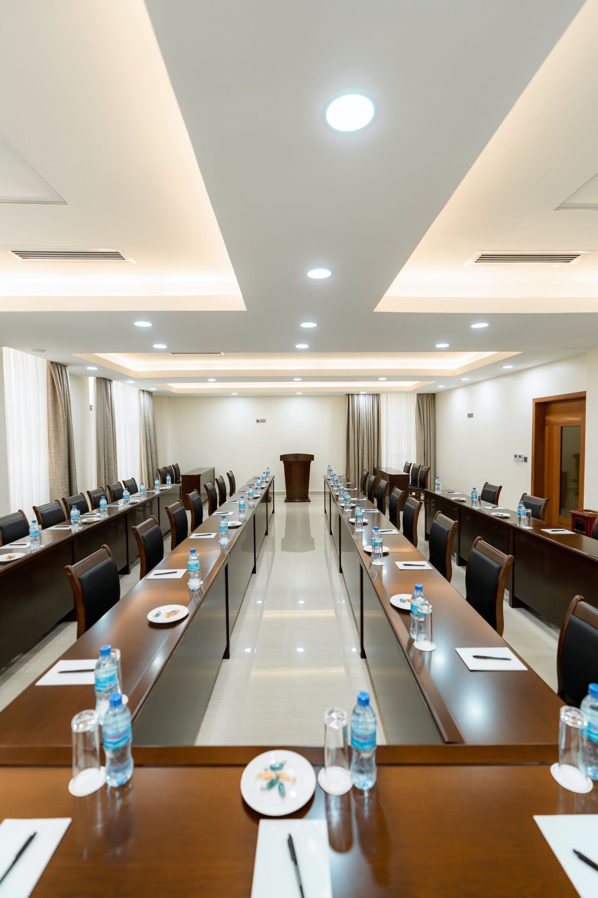 A conference room with long tables, chairs, water bottles, and a podium.