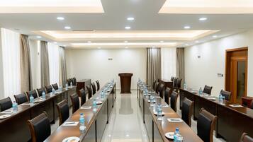 Un salón de conferencias con largas mesas, sillas, botellas de agua y un atril.