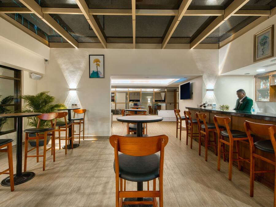 Un restaurante espacioso con sillas y mesas de madera, una zona de bar y un diseño de techo moderno.