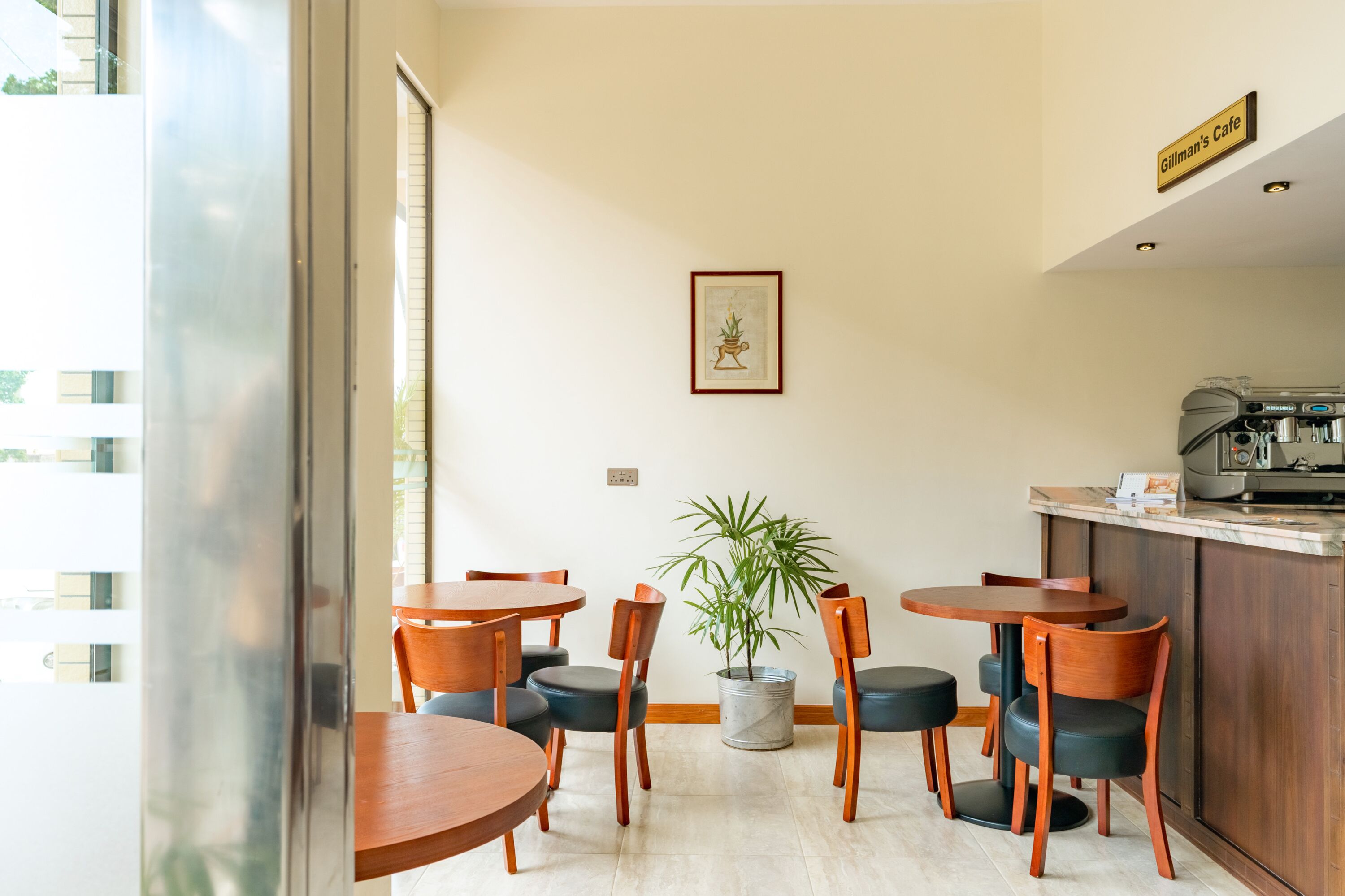 A cafe with wooden tables and chairs, a potted plant, and a coffee machine.