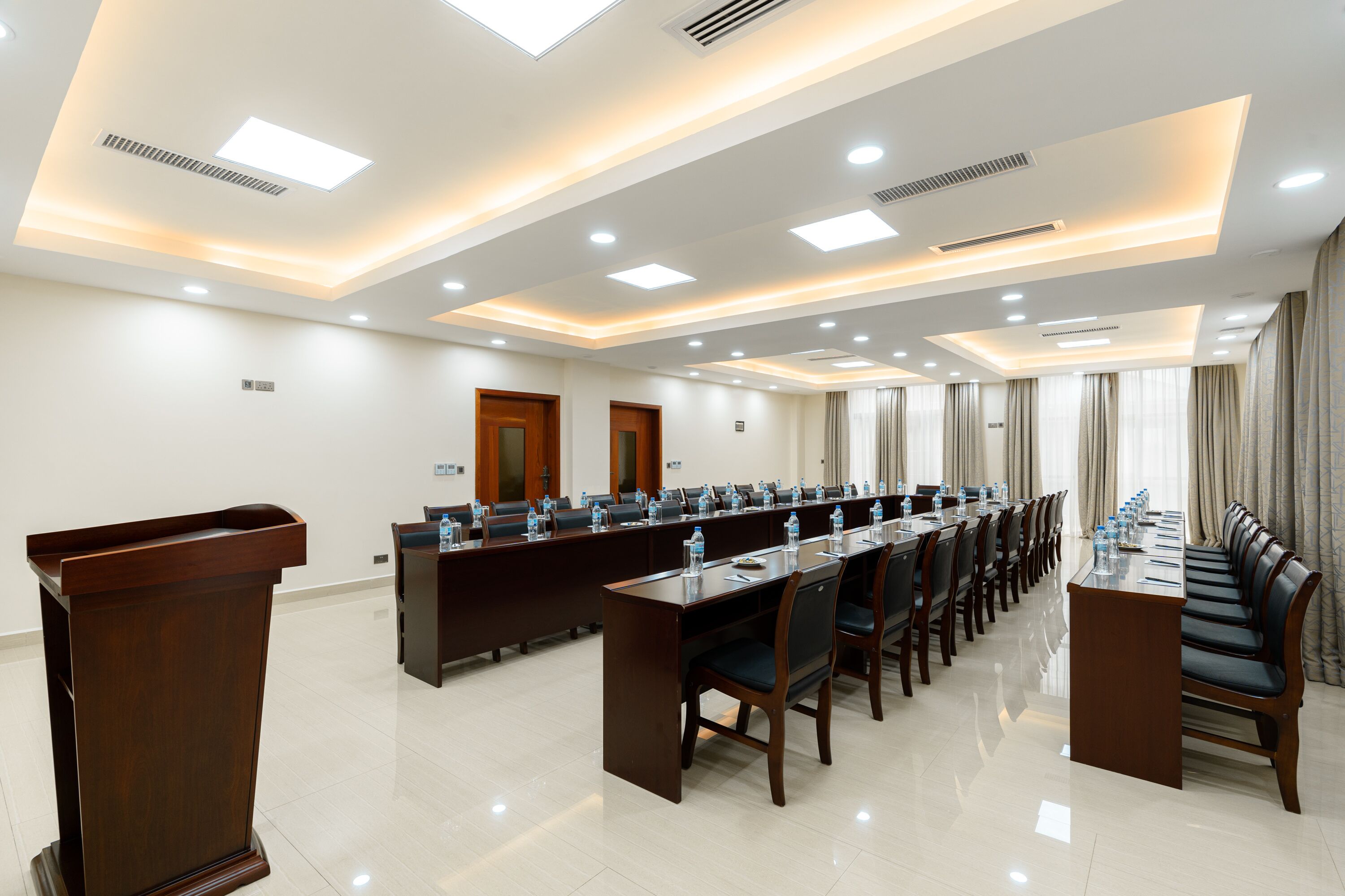 A conference room with a long table, chairs, a podium, and a ceiling with recessed lighting.