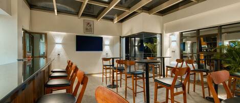 Un restaurante con sillas y mesas de madera, un separador de vidrio y un techo con vigas a la vista.