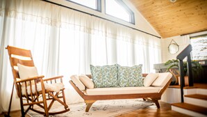A cozy living room with a rocking chair, a sofa with patterned cushions, and a large window with curtains.