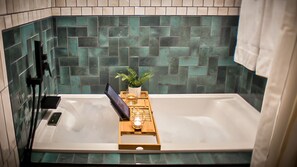 A bathroom with a bathtub, a wooden tray with a plant and a glass, and a towel hanging on the wall.