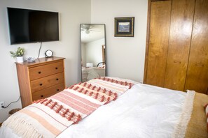 A bedroom with a bed, a dresser, a TV mounted on the wall, a mirror, and a wooden wardrobe.