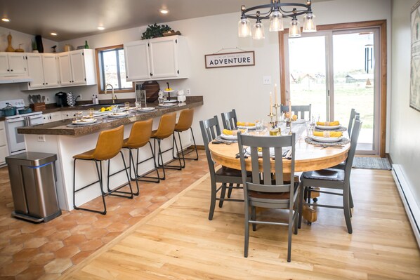A modern kitchen with a dining area, featuring a central island, bar stools, and a round table set for dining.