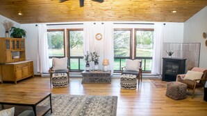 A spacious living room with wooden floors, large windows, a fireplace, and a cozy seating area.