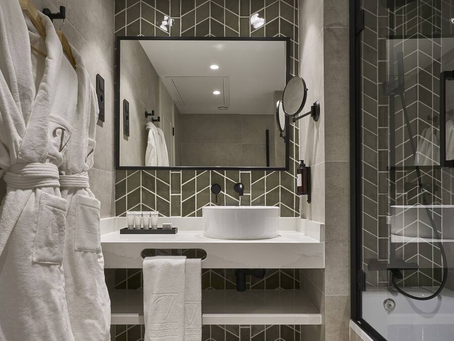 A modern bathroom with a vanity, a large mirror, a shower area, and a robe hanging on a rack.