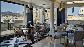 A modern dining area with tables and chairs, large windows with a city view, and hanging pendant lights. - Hotel Vincci Larios Diez (Málaga)