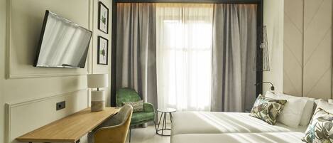 Habitación de hotel con cama, escritorio, silla, televisor y ventana con cortinas.