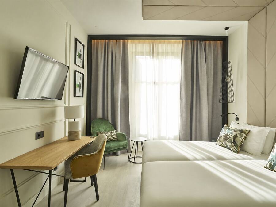 A hotel room with a bed, a desk, a chair, a TV, and a window with curtains.