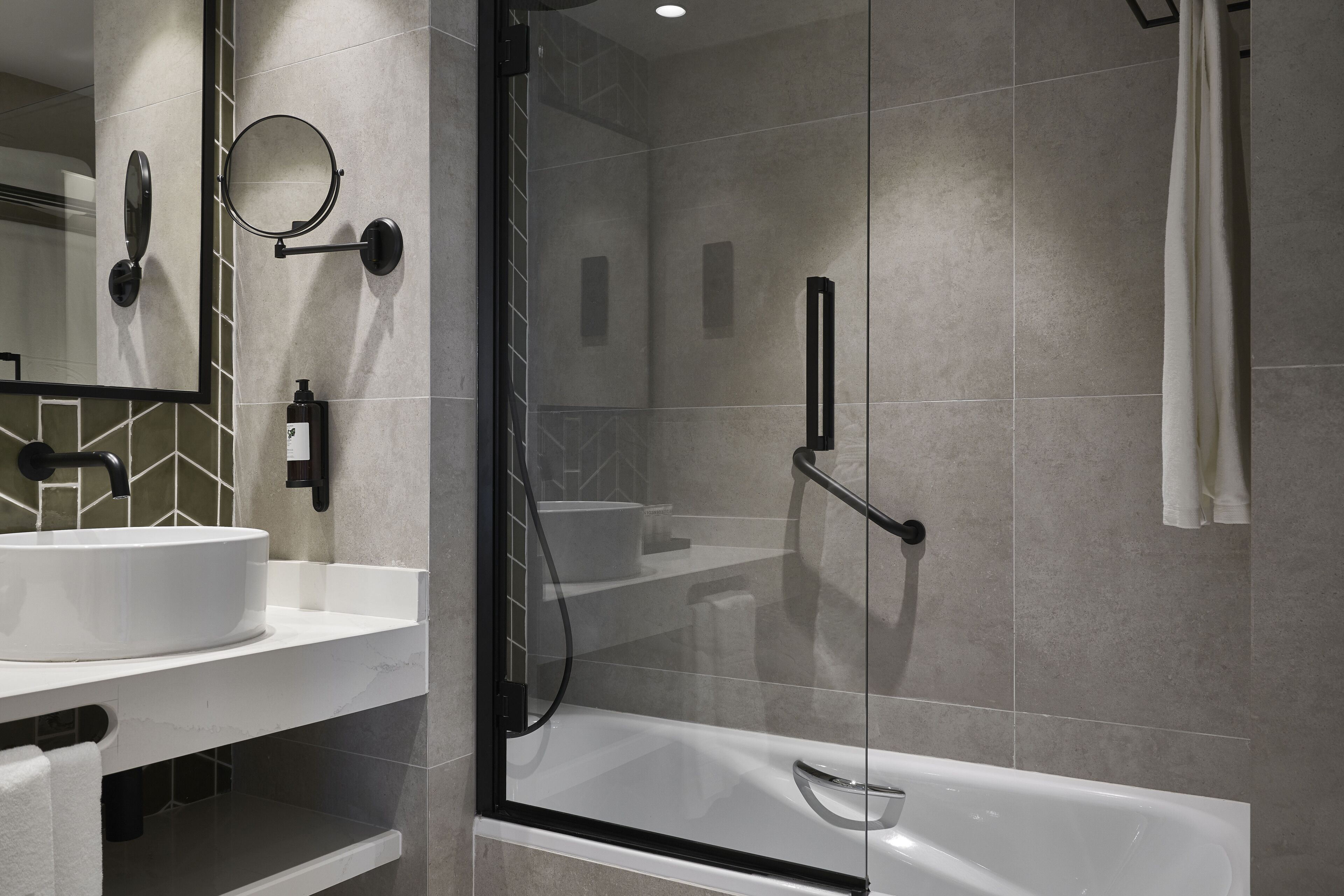 A modern bathroom with a glass-enclosed shower, a white sink, and a large mirror.