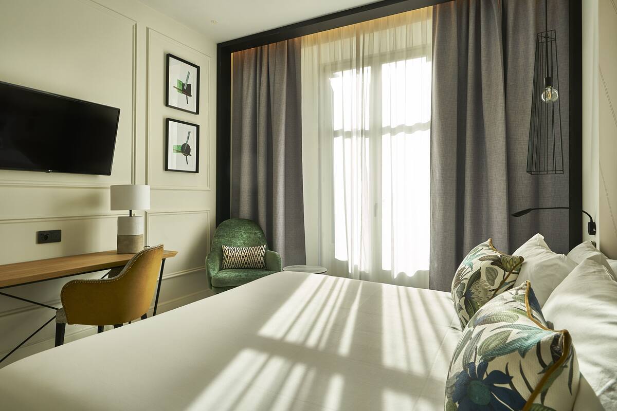 A hotel room with a bed, a desk, a chair, a TV, and curtains.