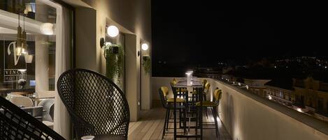 A balcony with a dining table and chairs, a chair with a cushion, and a hanging light fixture.