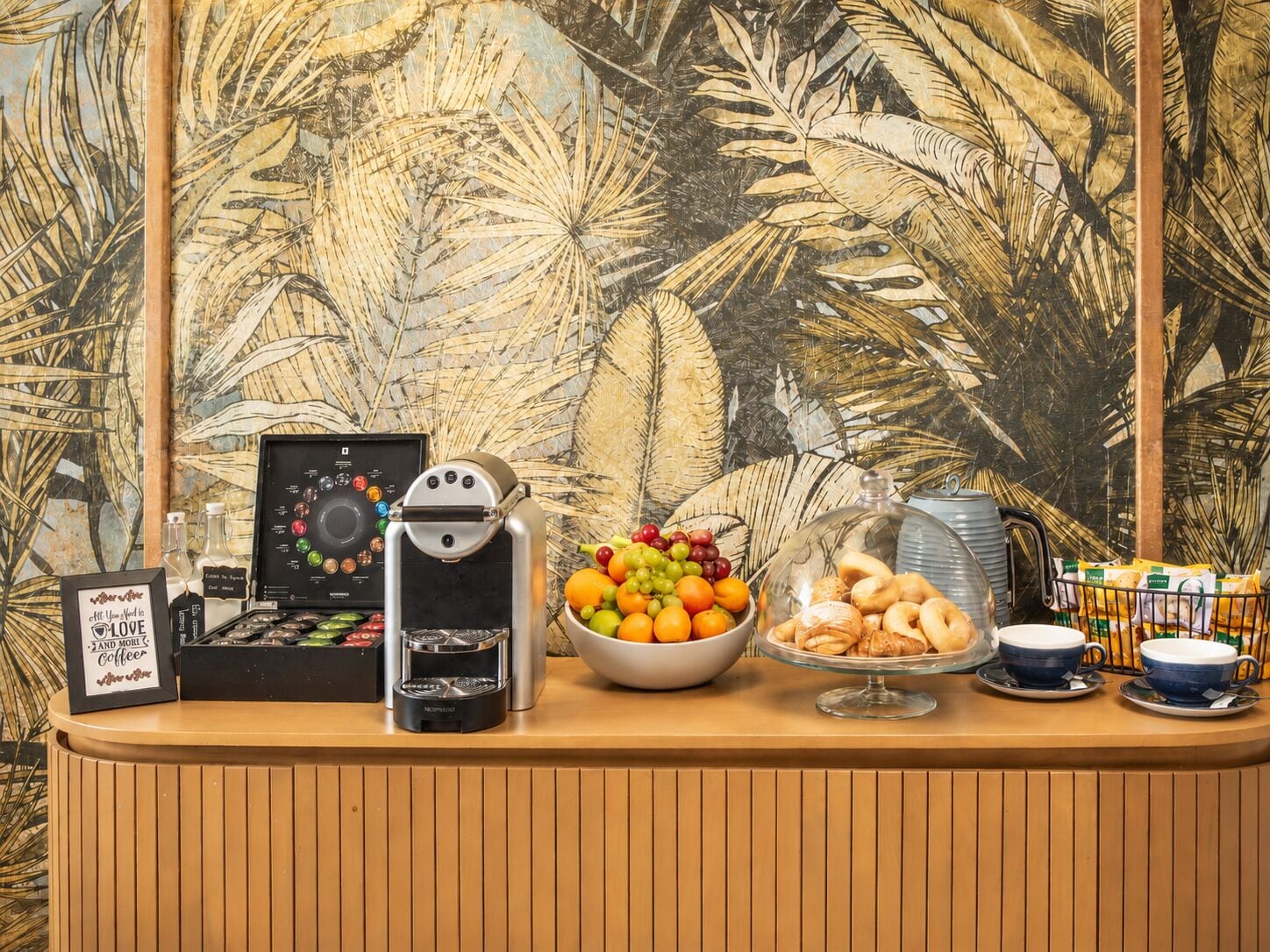 A coffee station with a coffee machine, a bowl of fruit, and pastries.