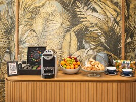 A coffee station with a coffee machine, a bowl of fruit, and pastries.